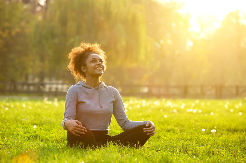 Photo of smiling woman sitting on grass with legs crossed